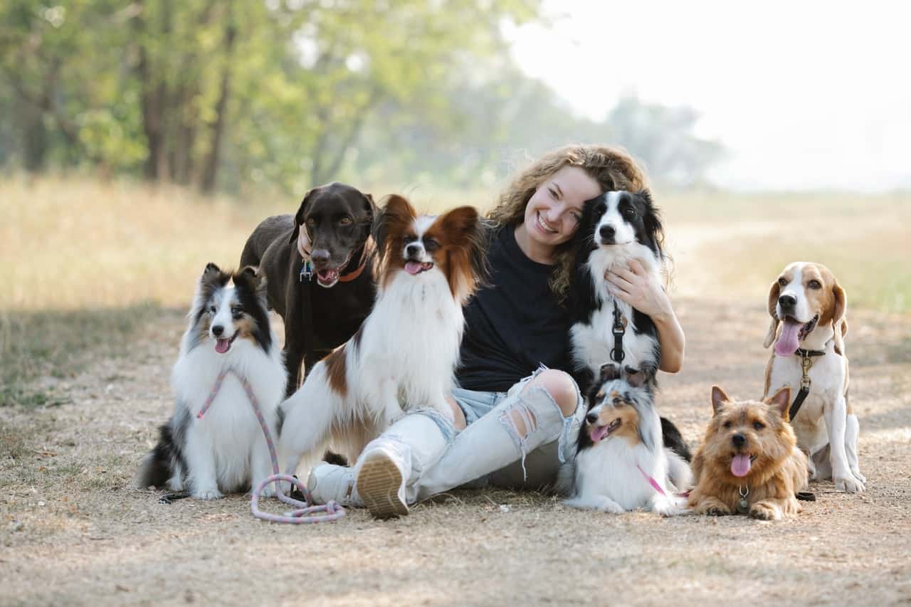 smiling woman with dogs embracing while sitting on ground